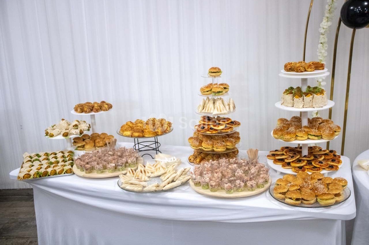 Buffet de pâtisseries et amuse-bouches variés disposés sur des présentoirs et une table blanche.