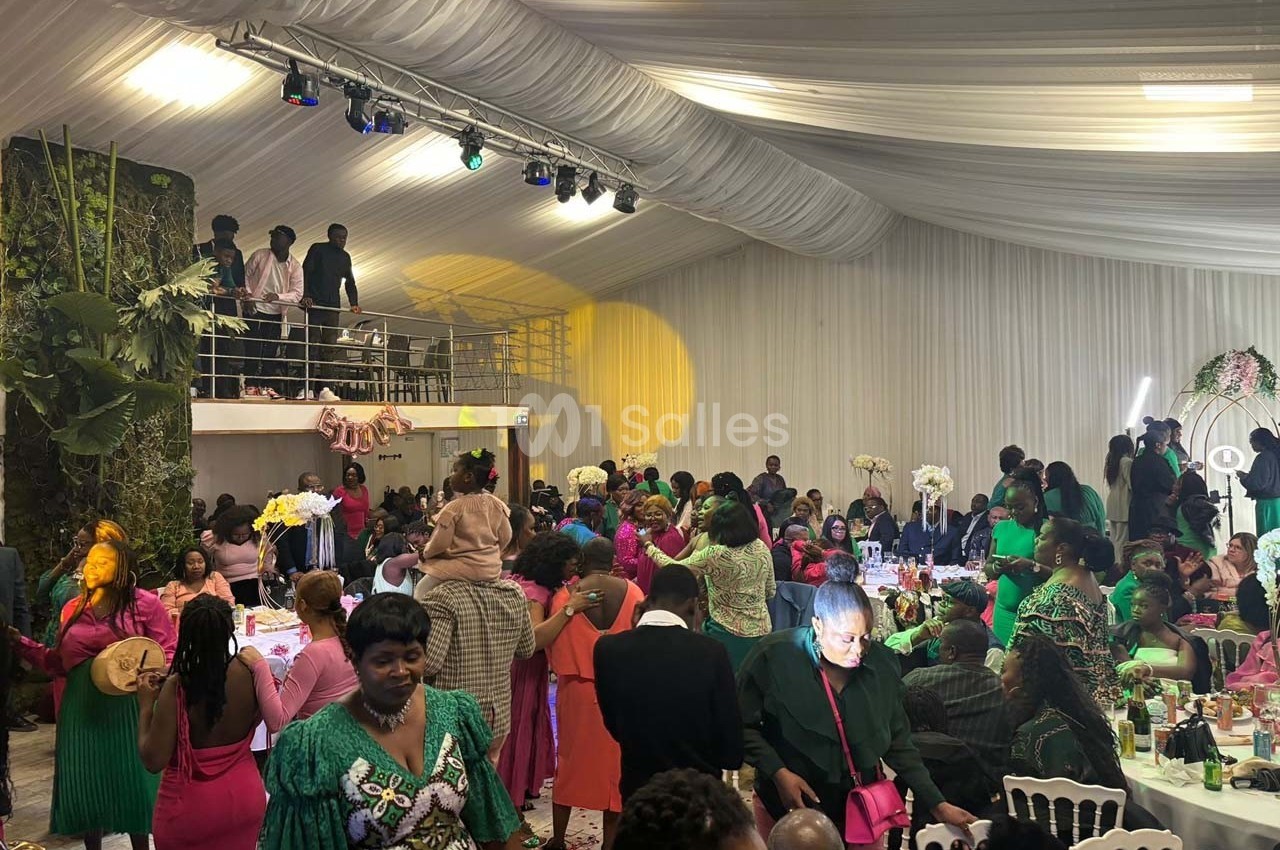Des invités vêtus de tenues colorées participent à une réception festive dans une salle décorée avec des fleurs et des…