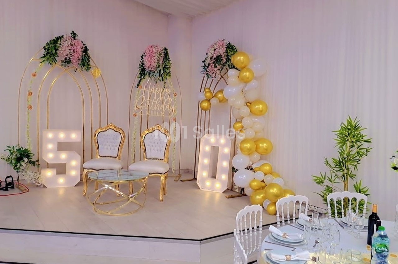 Décoration de fête avec deux fauteuils dorés, ballons blancs et dorés, et chiffres lumineux ’50’ sur une estrade.