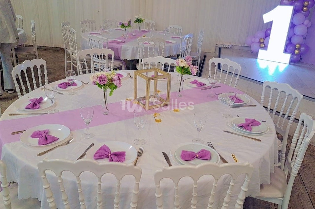 Table décorée pour un événement avec nappes blanches, chemins de table roses, serviettes pliées et centre de table floral.