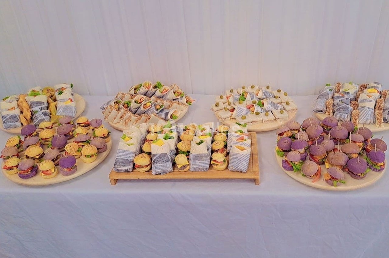 Plateaux variés de petits sandwichs et amuse-bouches colorés disposés sur une table blanche.