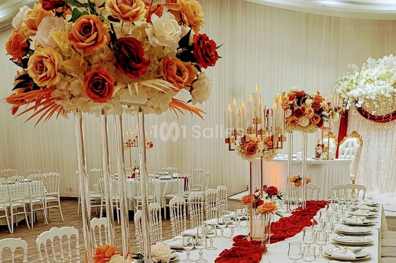 Salle de réception décorée avec des compositions florales aux tons chauds, nappes blanches et chandeliers élégants.