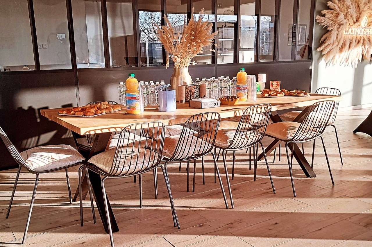 Table en bois dressée avec des boissons, viennoiseries et décorations de pampas, entourée de chaises métalliques.