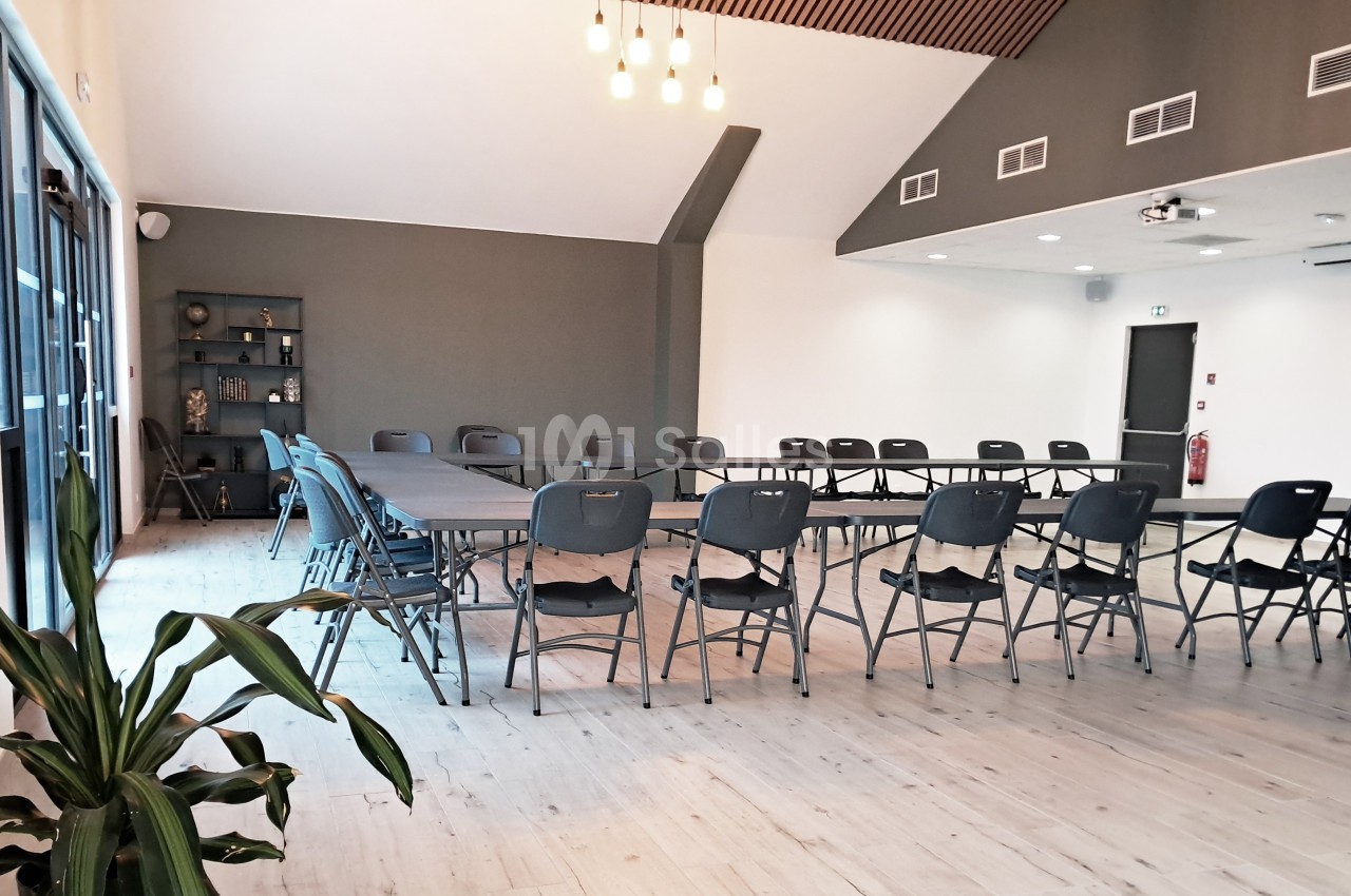 Salle de réunion lumineuse avec des tables disposées en U, des chaises pliantes et une décoration sobre.