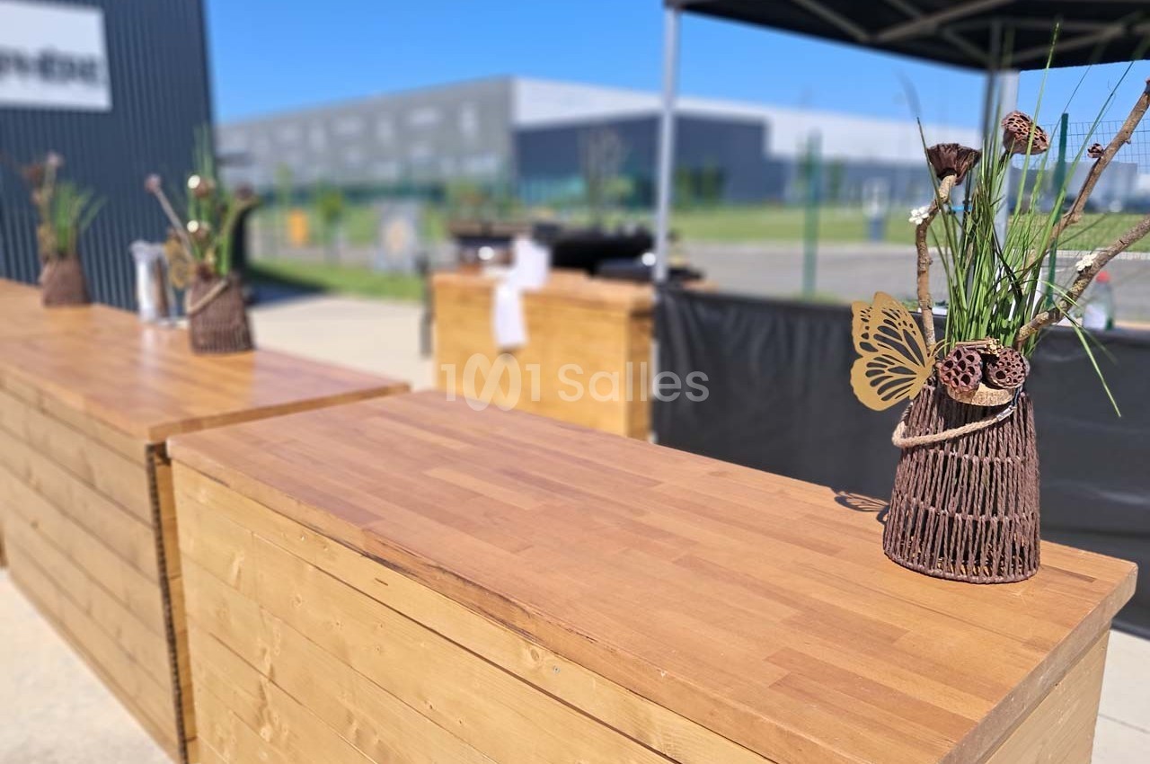Comptoirs en bois avec décorations florales, installés en extérieur sous un ciel dégagé près de bâtiments modernes.