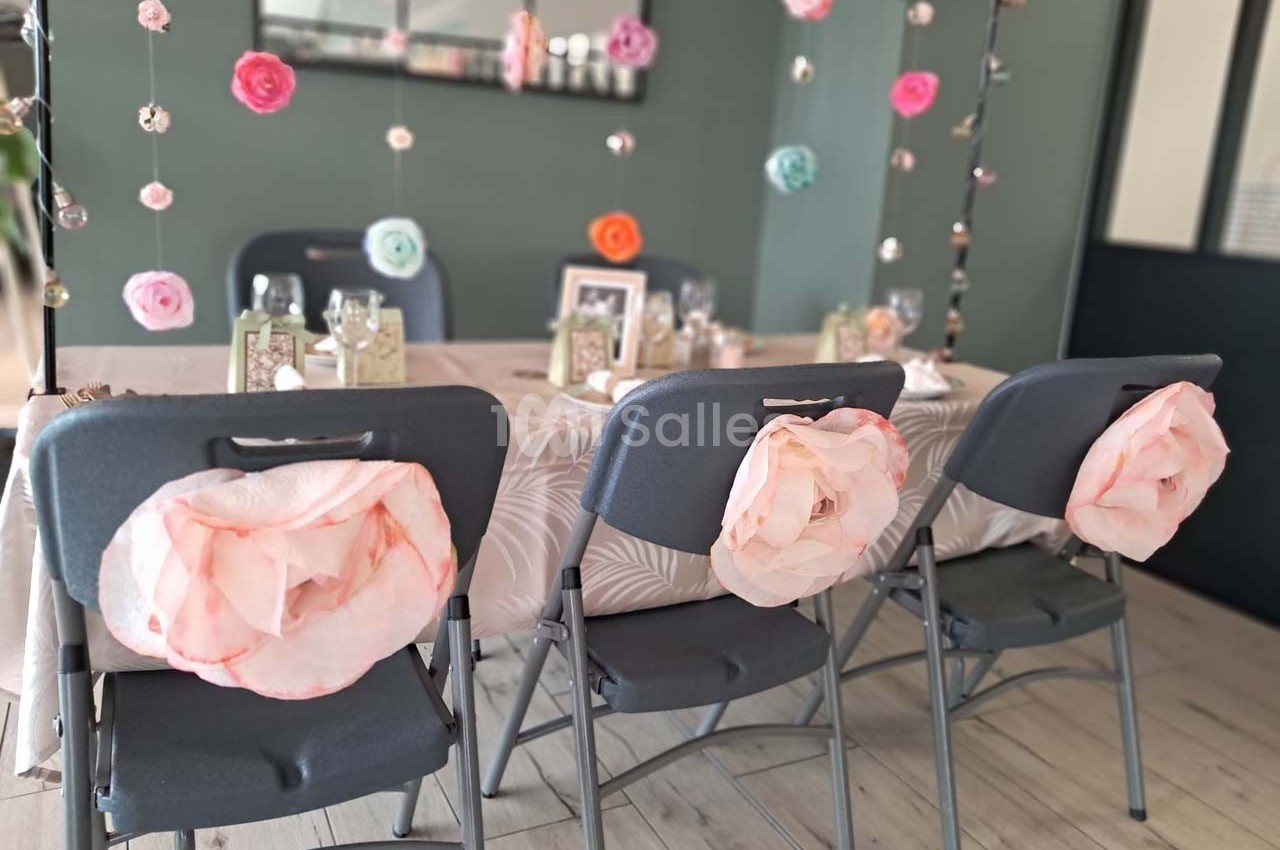Table décorée pour une fête avec des fleurs suspendues et des chaises ornées de grandes fleurs en papier rose.