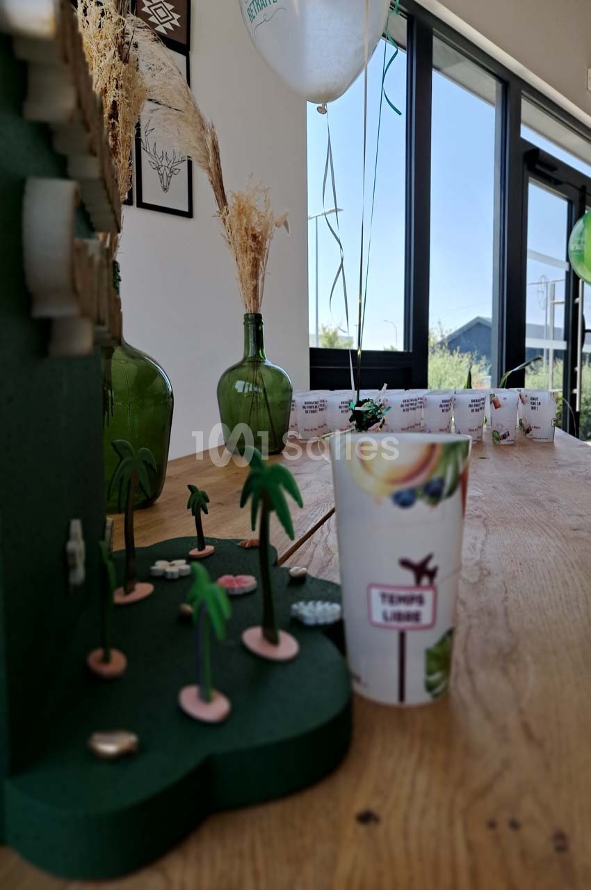 Décoration de table avec des gobelets, des ballons, des plantes miniatures et des vases près d'une fenêtre lumineuse.