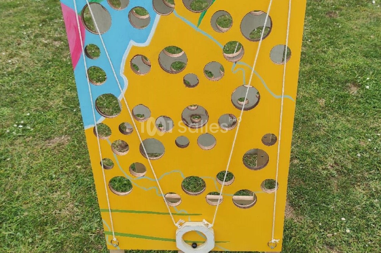 Panneau en bois jaune percé de trous, représentant un fromage, utilisé pour un jeu en plein air sur une pelouse.