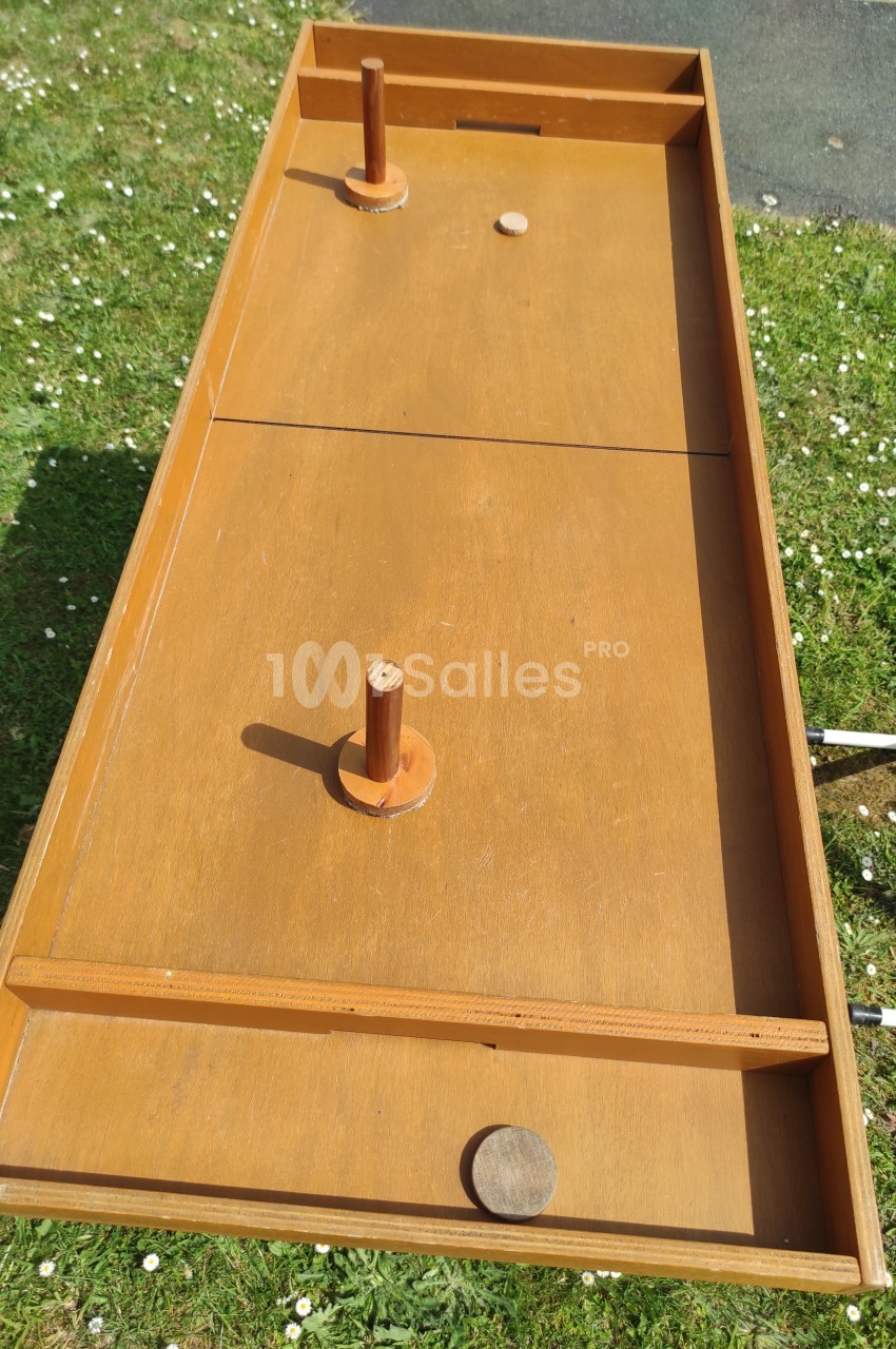 Jeu en bois traditionnel avec deux manches et un palet, posé sur une pelouse en extérieur.