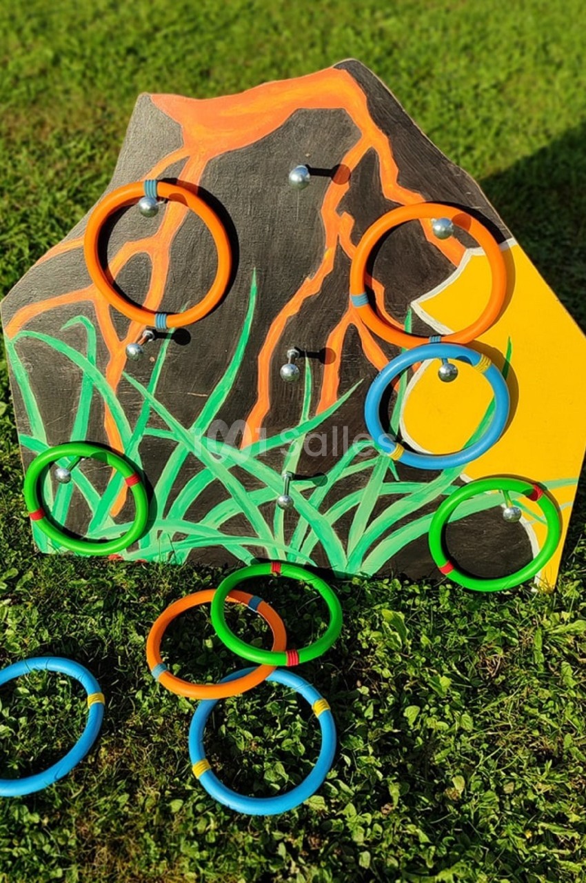 Panneau en bois coloré avec des anneaux multicolores accrochés et posés sur de l'herbe.
