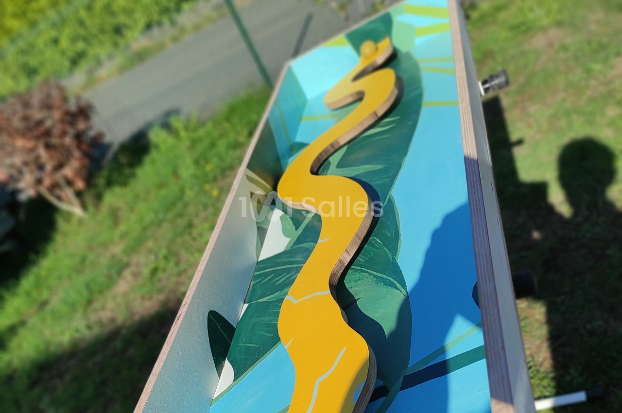 Planche en bois peinte avec un motif de feuille tropicale et un chemin jaune sinueux, posée en extérieur.
