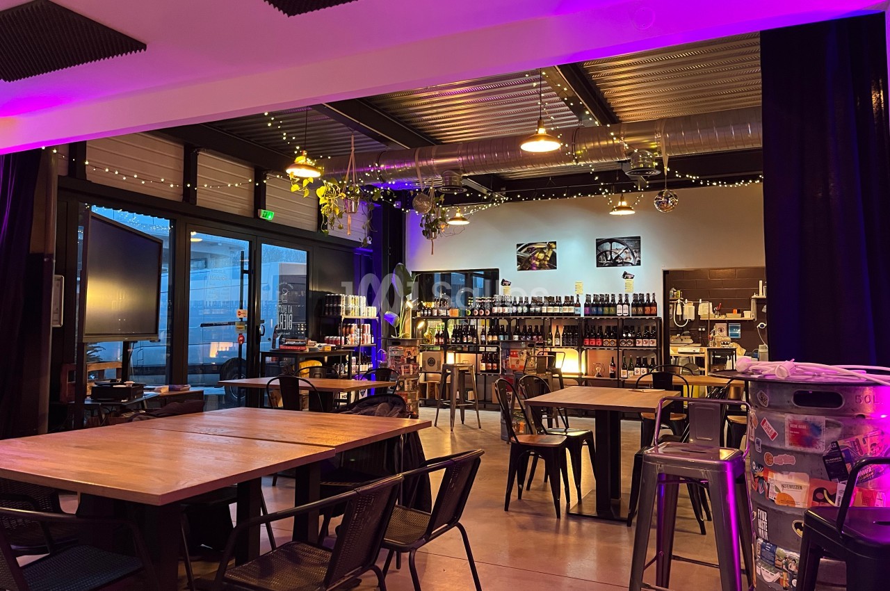 Salle moderne avec tables en bois, chaises métalliques, étagères de produits et éclairage chaleureux.