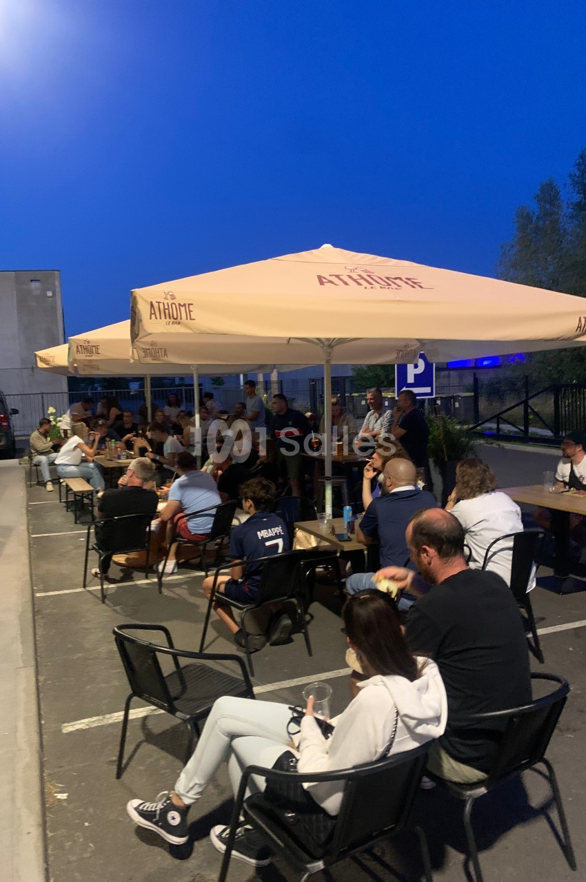 Des personnes assises en terrasse sous des parasols, partageant un moment convivial en soirée dans un espace extérieur.