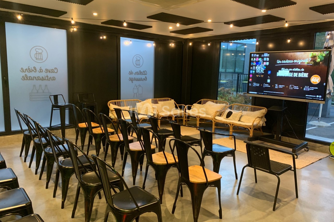 Salle de conférence moderne avec chaises alignées, canapés en rotin et écran affichant une présentation.