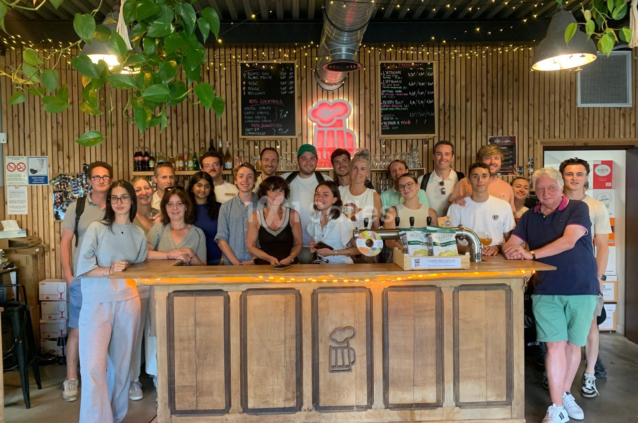 Un groupe de personnes souriantes posant derrière un comptoir en bois dans un bar décoré de plantes et lumières.