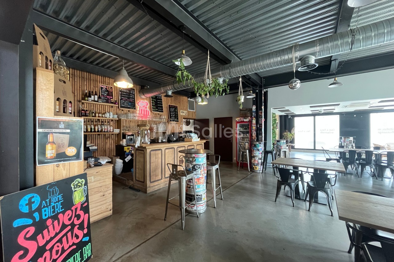 Intérieur d'un bar avec comptoir en bois, tables, chaises métalliques et décoration industrielle.