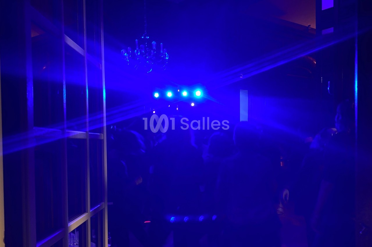 Foule dans une salle sombre éclairée par des lumières bleues vives, avec un lustre visible au plafond.