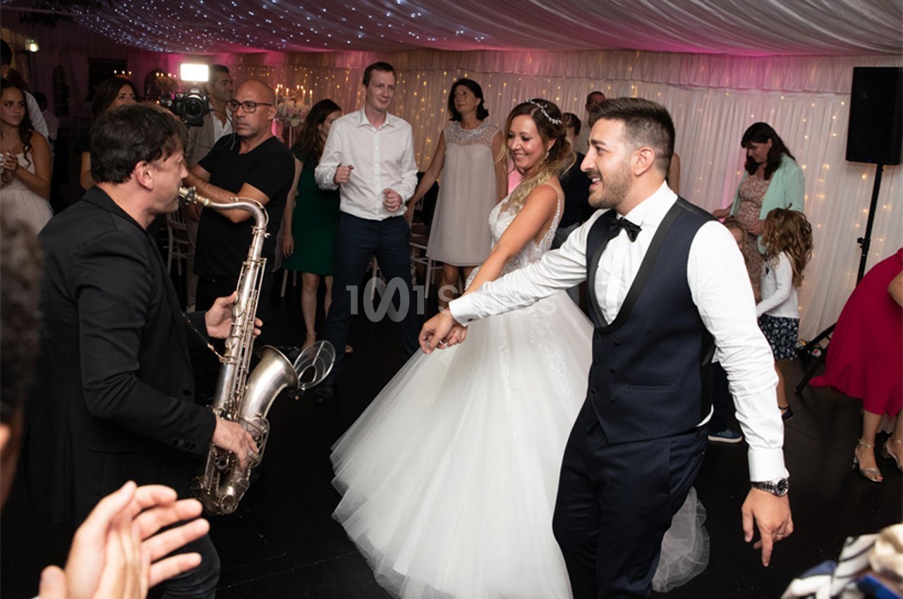 Un saxophoniste joue lors d'une réception de mariage, entouré d'invités dansant sous un plafond illuminé.
