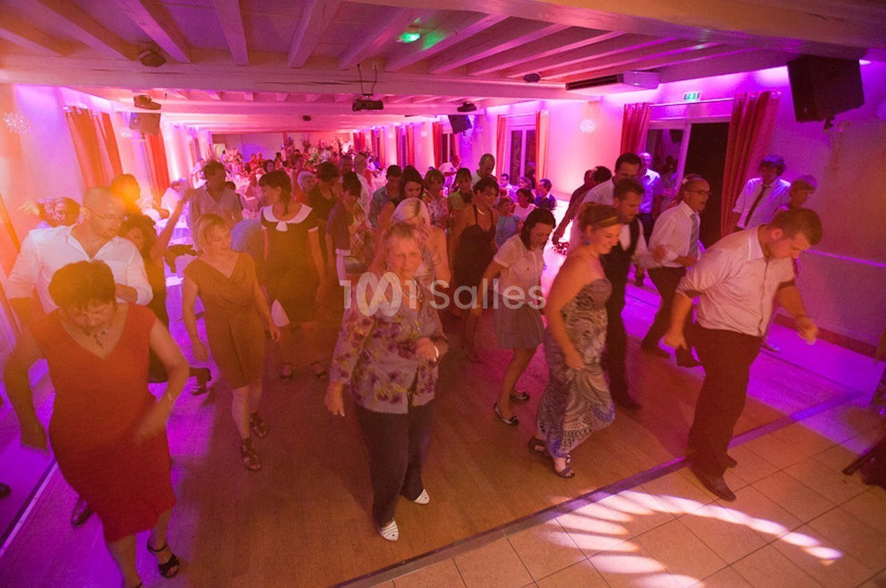 Personnes dansant en groupe dans une salle éclairée par des lumières colorées, ambiance festive et conviviale.