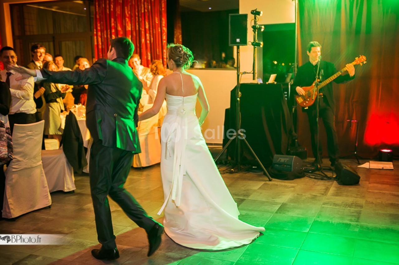 Un couple danse lors d'une réception, accompagné d'un musicien jouant de la basse en arrière-plan.