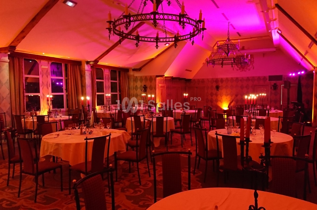 Salle de réception décorée avec des tables rondes, des chandeliers allumés et un éclairage tamisé aux tons chauds.