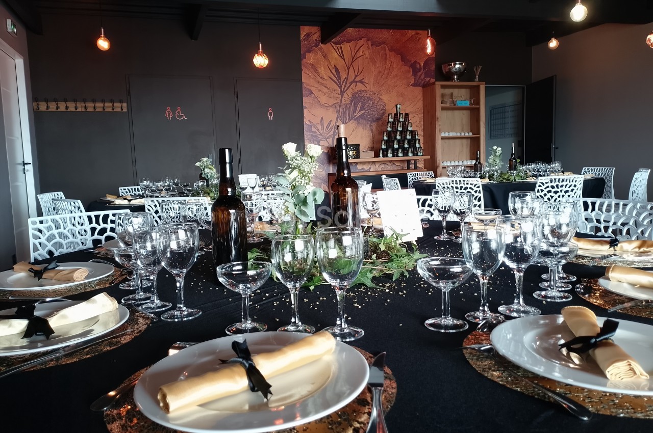 Table élégamment dressée avec nappes noires, vaisselle raffinée, décor floral et bouteilles de vin dans une salle sombre.
