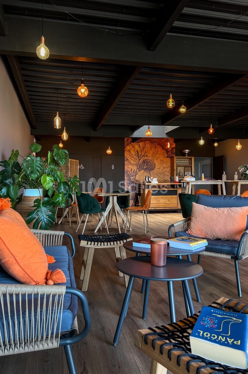 Espace de détente moderne avec fauteuils en rotin, tables basses, plantes et éclairage suspendu chaleureux.