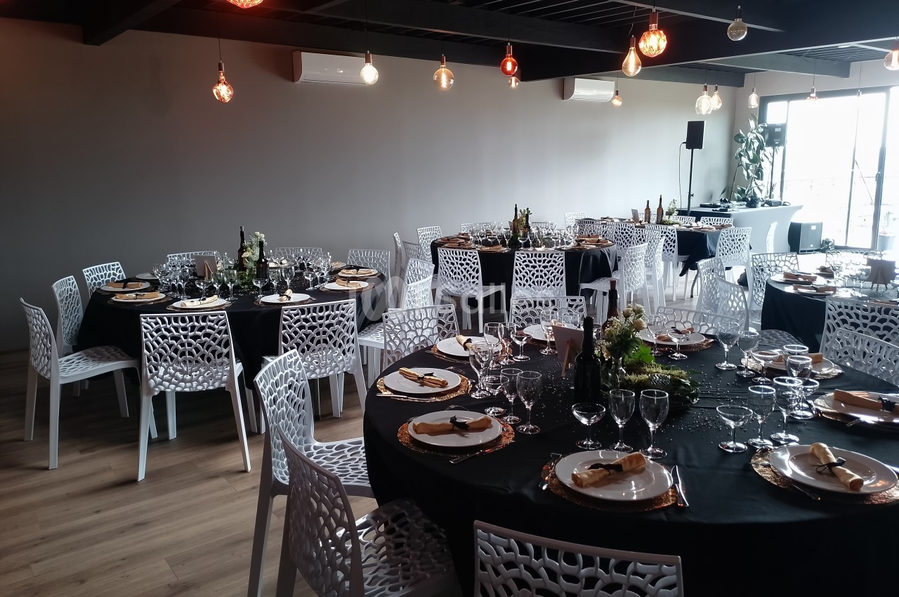 Salle de réception avec tables rondes dressées, nappes noires, chaises blanches ajourées et décorations élégantes.