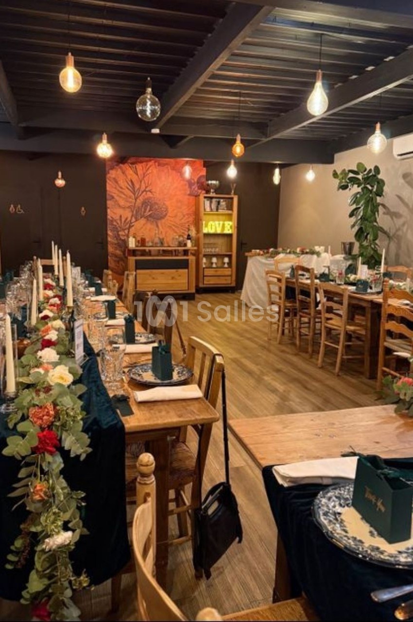 Salle de réception décorée avec des tables dressées, guirlandes florales et éclairage chaleureux.