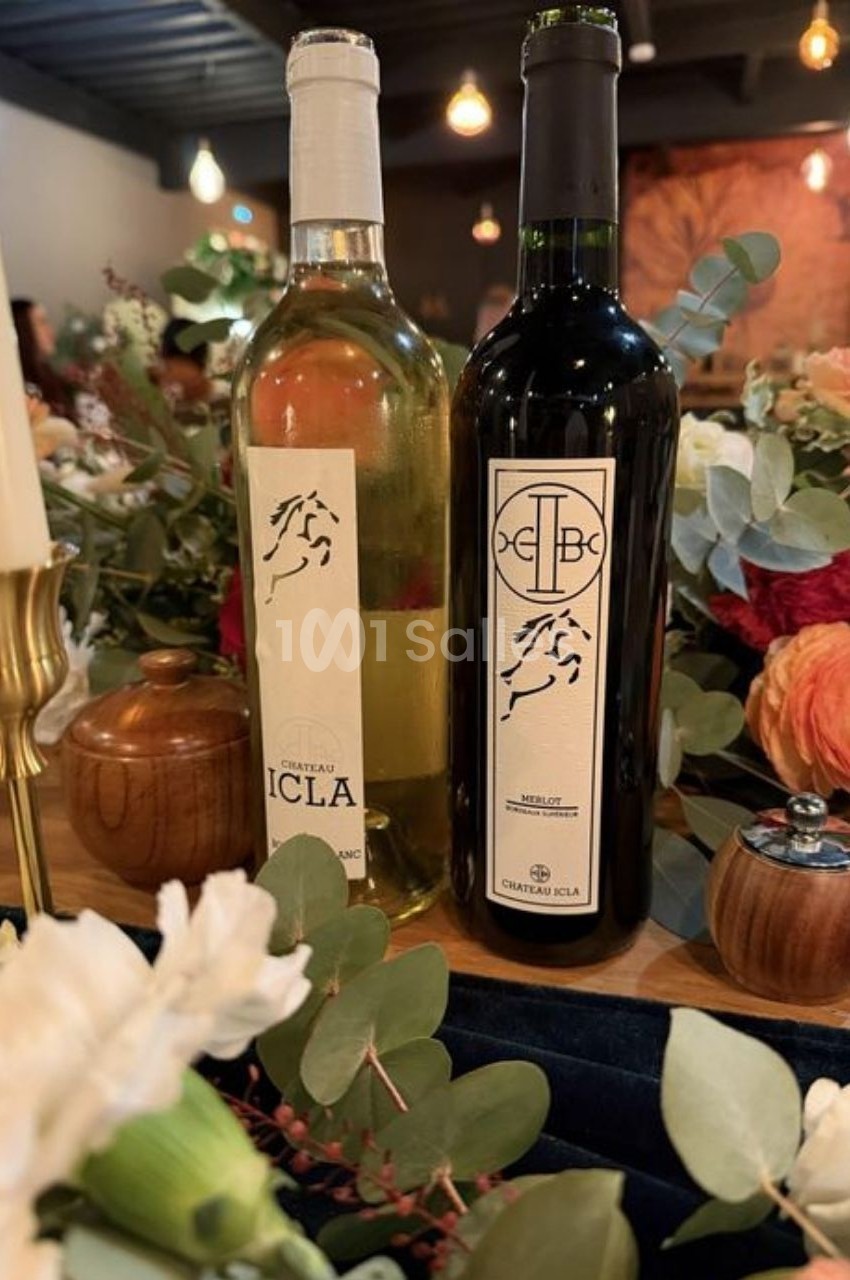Deux bouteilles de vin, blanc et rouge, posées sur une table décorée de fleurs et de feuillage.