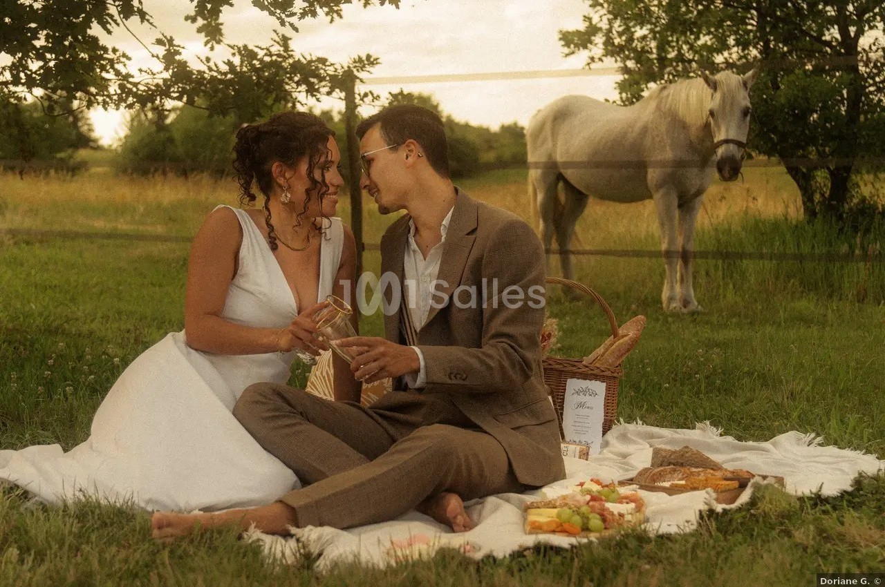 Un couple assis sur une couverture lors d'un pique-nique champêtre, avec un cheval en arrière-plan.
