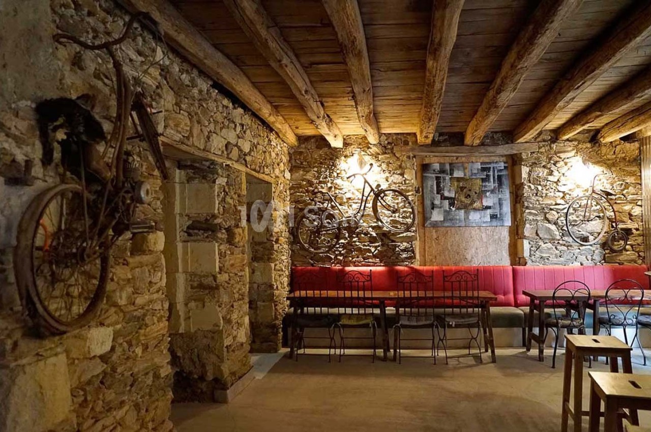 Salle rustique avec murs en pierre, plafond en bois, vélos accrochés et mobilier en métal et bois.