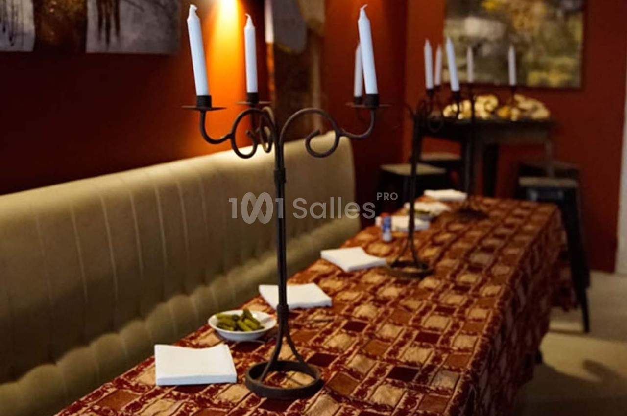 Deux chandeliers à bougies décorent une table recouverte d'une nappe rouge dans un intérieur chaleureux.