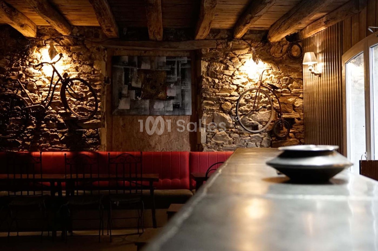Intérieur rustique avec murs en pierre, vélos accrochés, banquettes rouges et éclairage chaleureux.