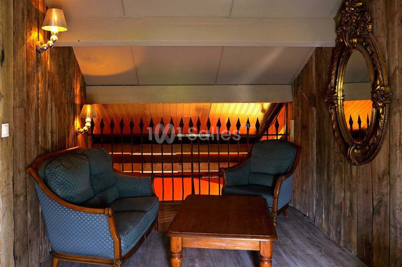 Deux fauteuils et une table basse en bois dans un espace rustique avec murs en bois, miroir doré et éclairage chaleureux.