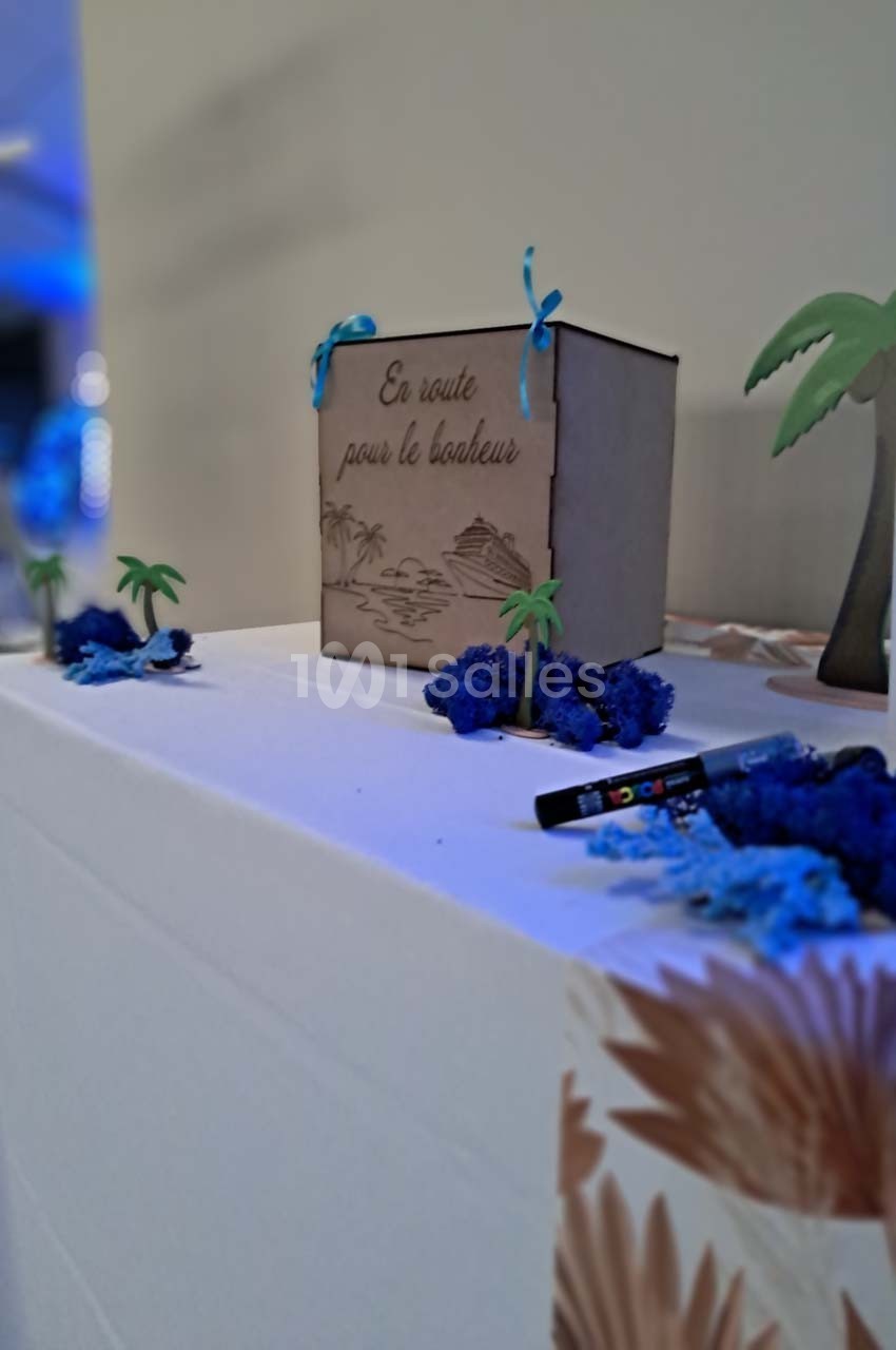 Boîte décorative en bois gravée ’En route pour le bonheur’, entourée de mini-palmiers et de décorations bleues.