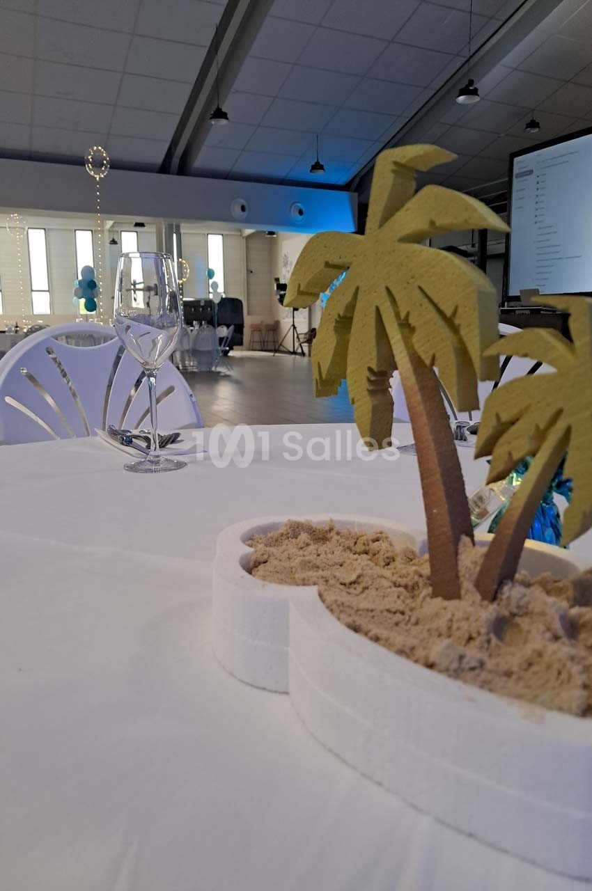 Centre de table avec des mini-palmiers sur du sable, posé sur une table blanche dans une salle décorée.