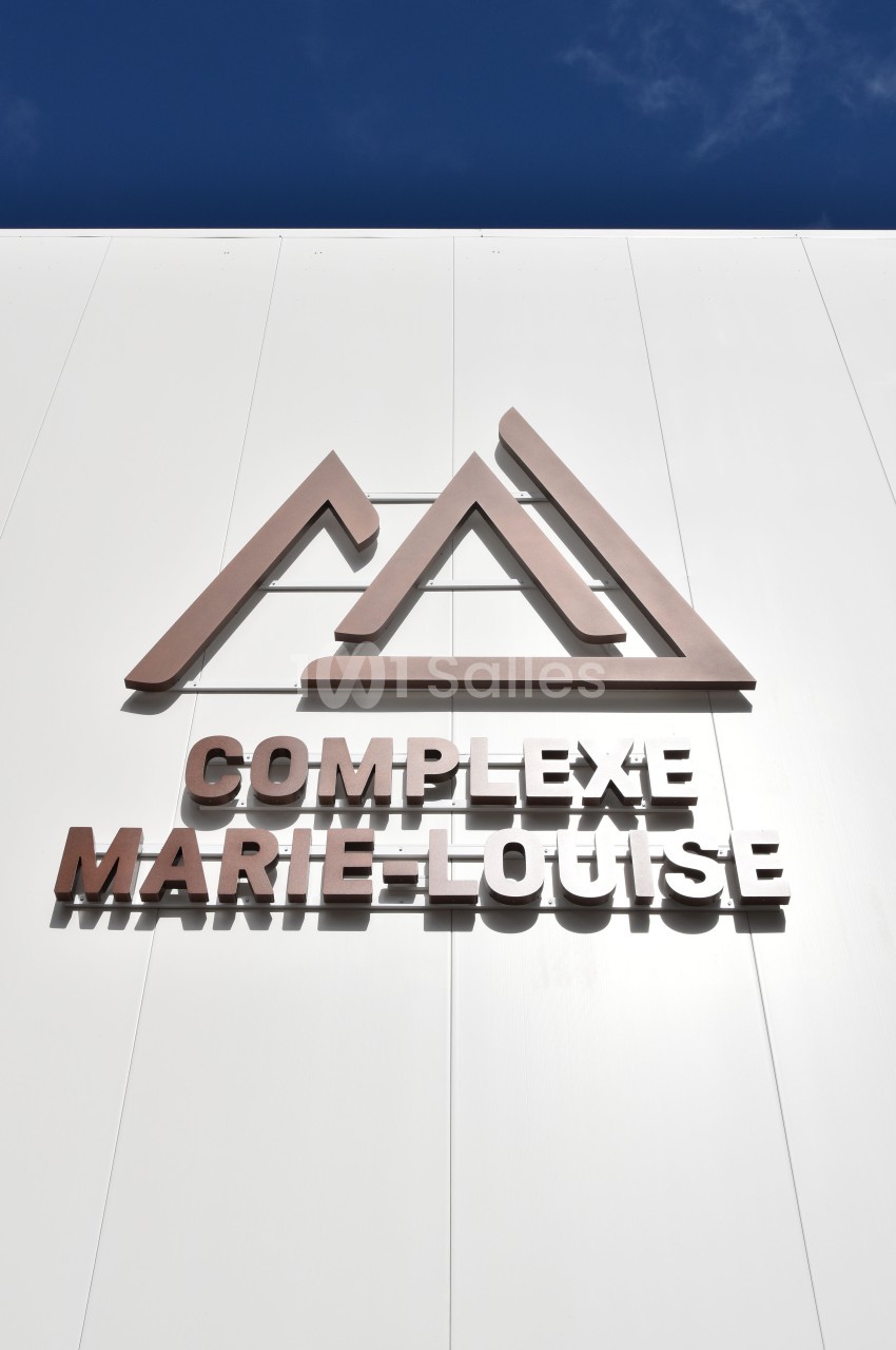 Façade blanche avec le logo et le nom ’Complexe Marie-Louise’ en lettres métalliques sous un ciel bleu.