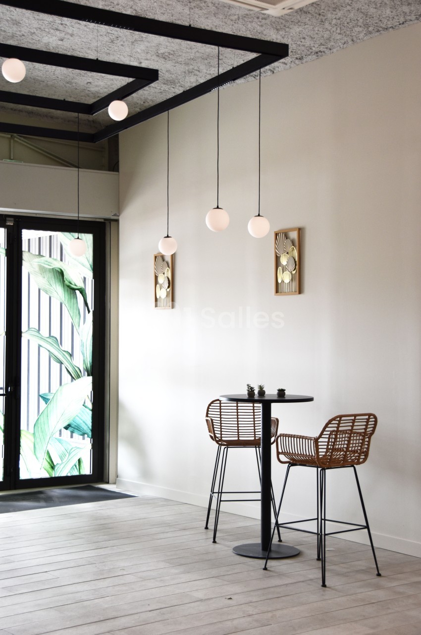 Deux chaises en rotin et une table haute noire dans un intérieur minimaliste avec des suspensions et des décorations murales.