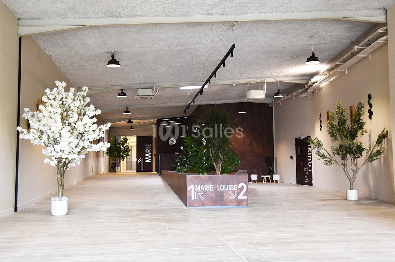 Entrée d'un espace intérieur moderne avec des plantes décoratives, un sol clair et un panneau indiquant deux directions.