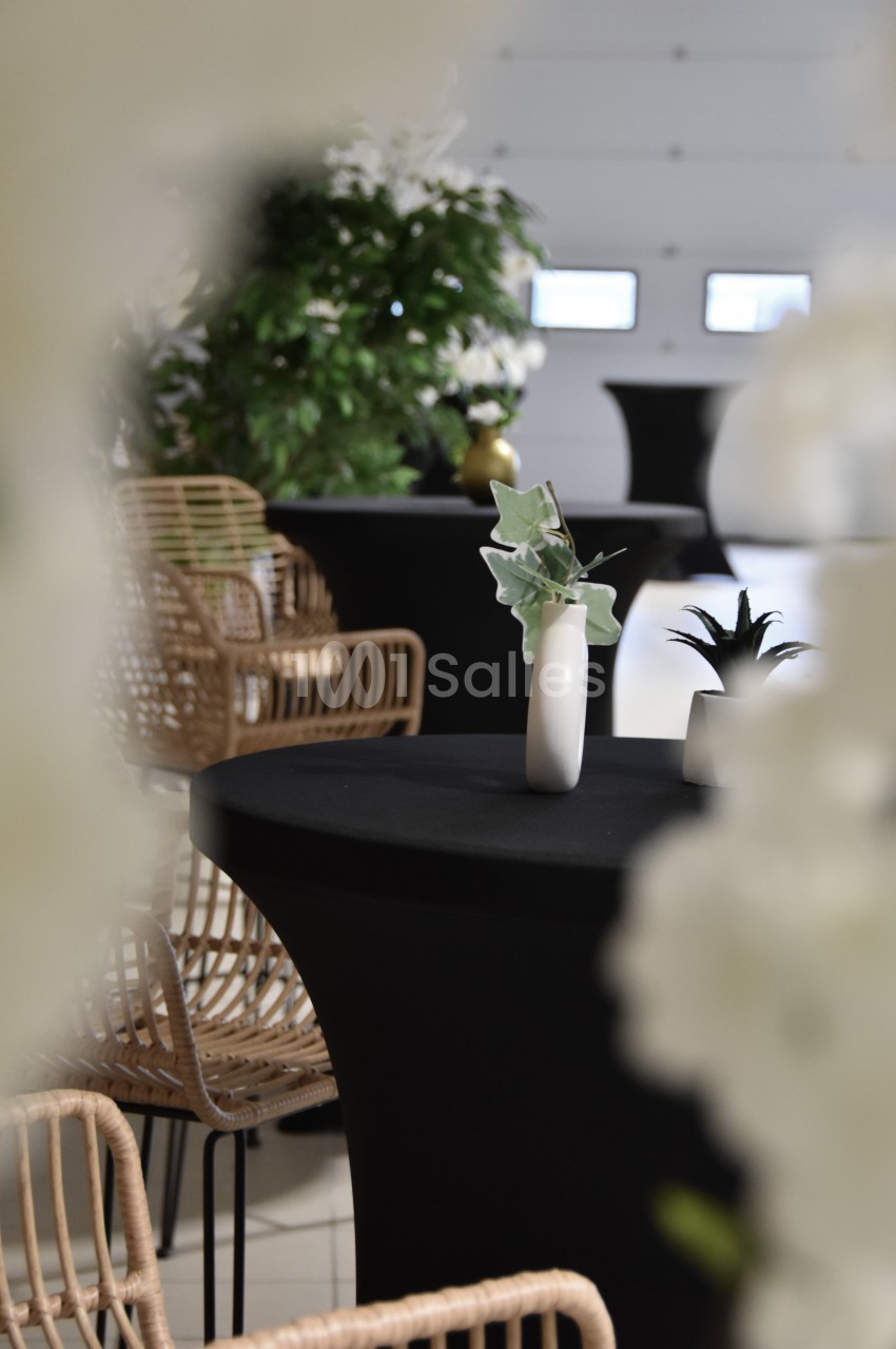 Tables hautes noires décorées de vases blancs et entourées de chaises en rotin dans un espace lumineux.