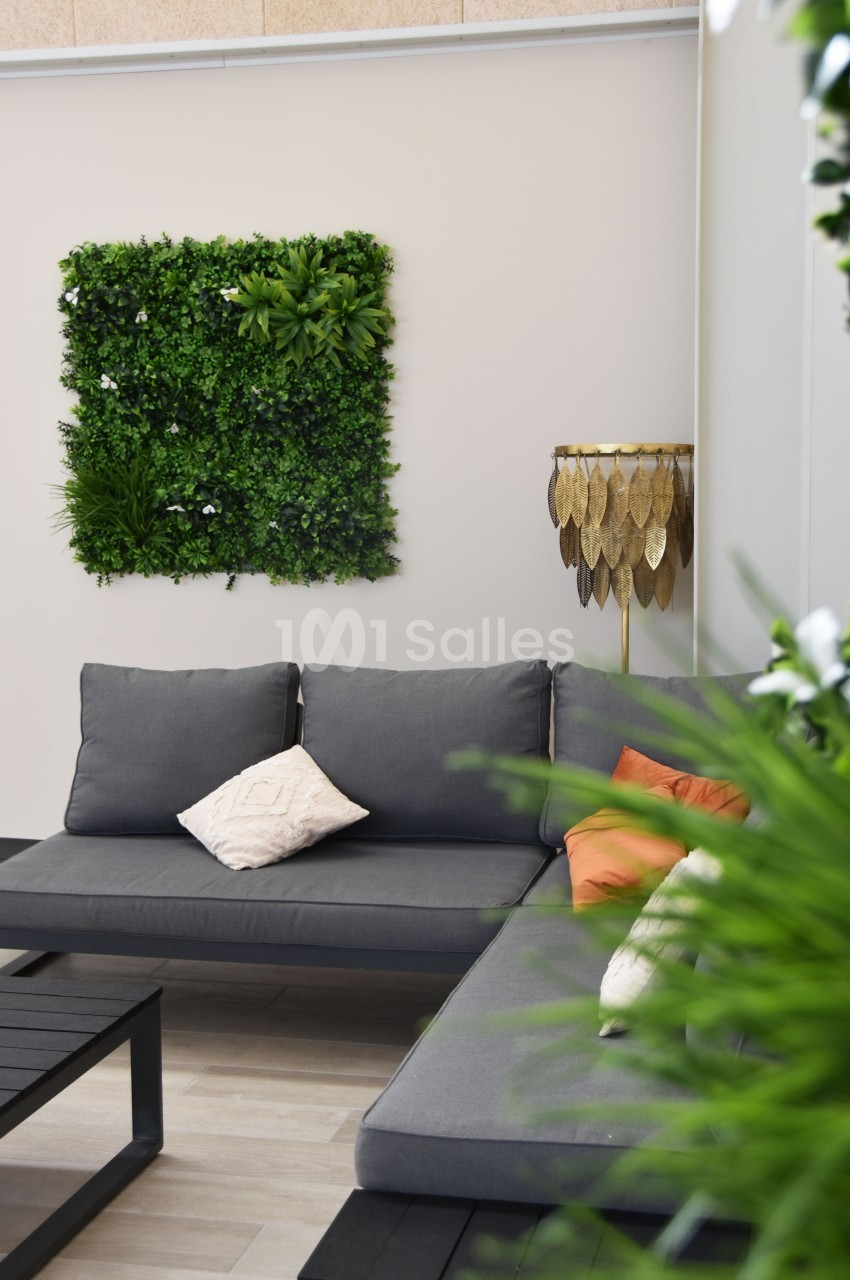Canapé gris avec coussins colorés, table basse noire et mur végétal décoratif dans un espace intérieur lumineux.