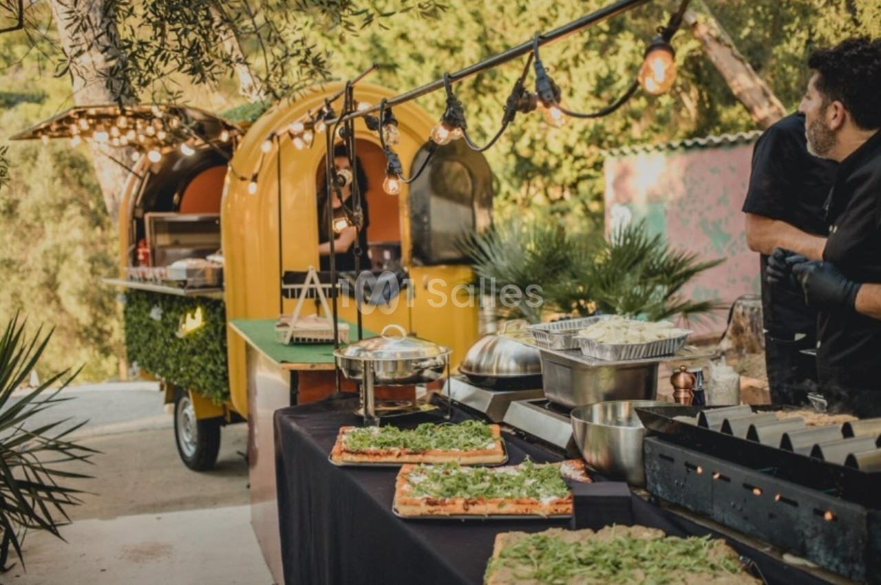 Food truck jaune avec guirlandes lumineuses, buffet de plats préparés et décoration végétale en extérieur.