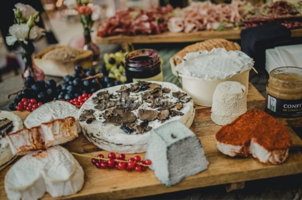 Plateau de fromages variés avec truffes, fruits rouges, raisins, confiture et charcuterie en arrière-plan.
