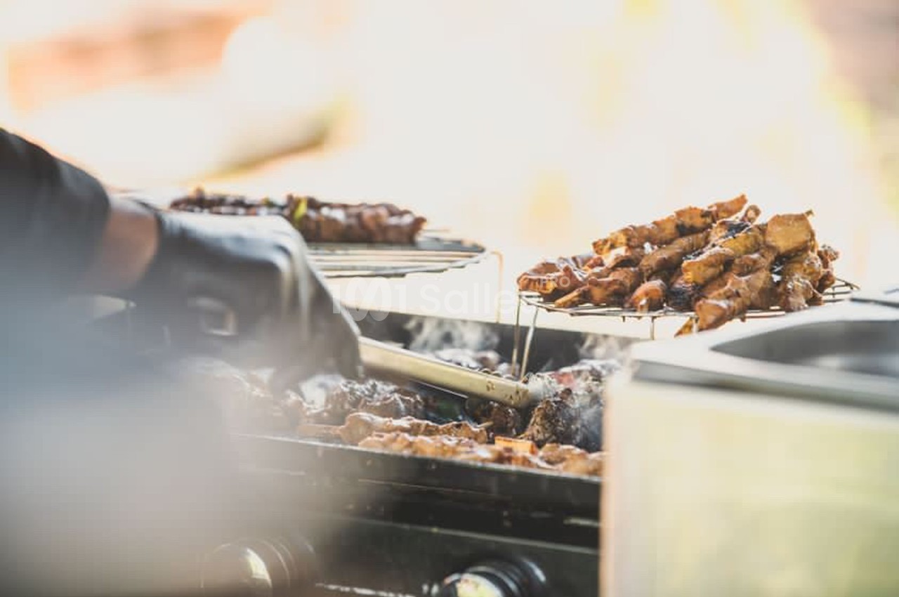 Personne en gant noir retournant des brochettes de viande grillées sur un barbecue en plein air.