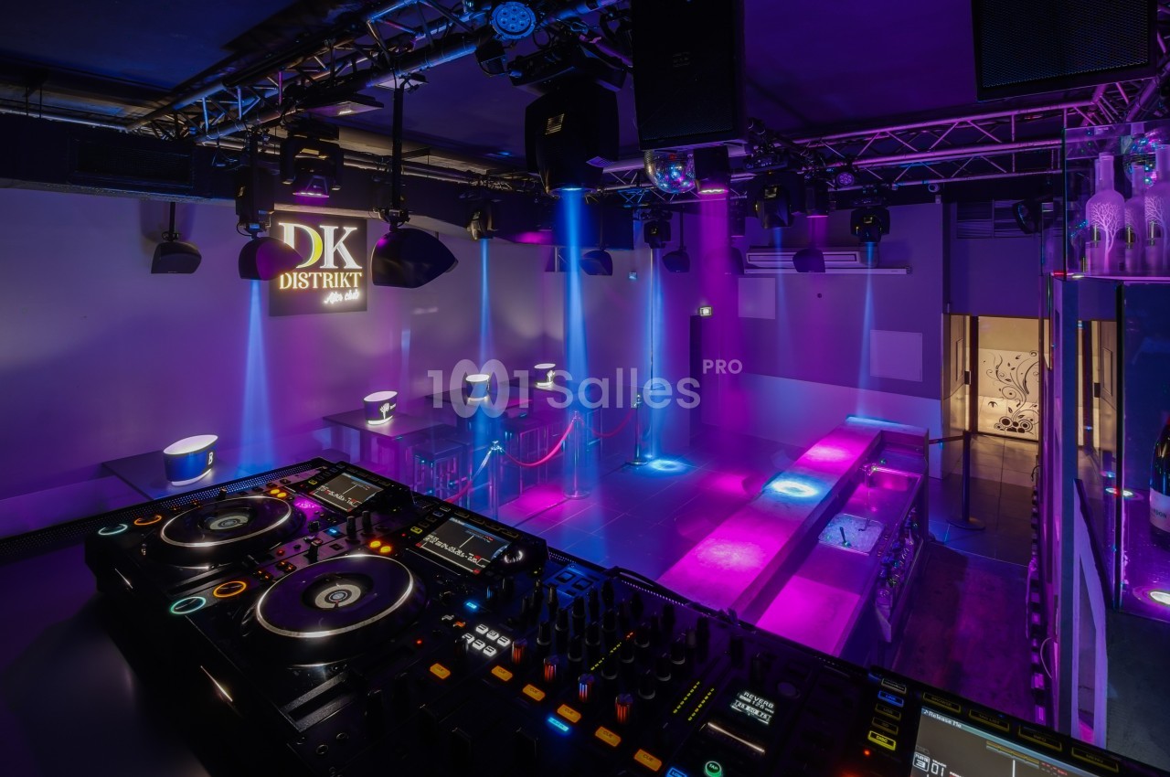 Salle de club avec piste de danse éclairée par des lumières colorées, vue depuis une table de mixage.