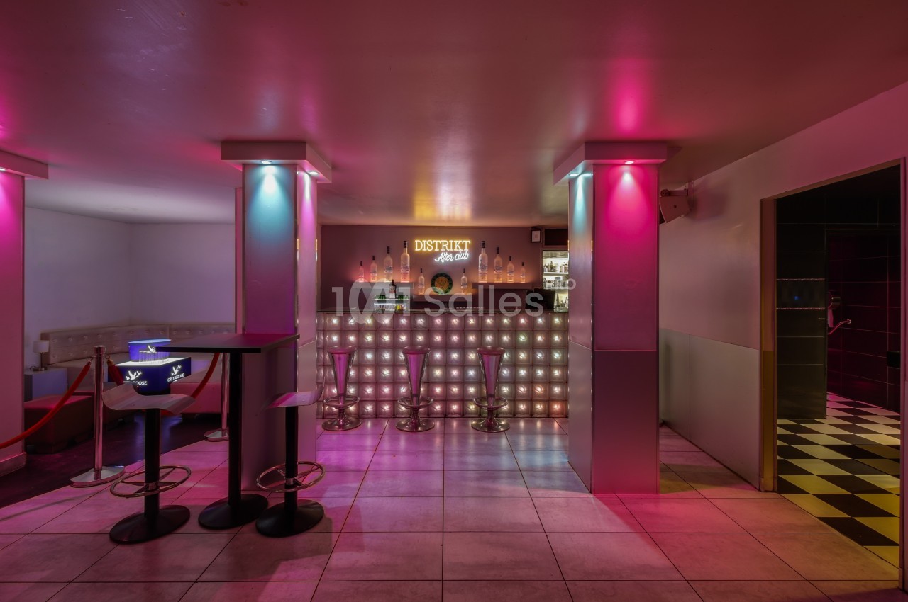 Bar lumineux avec tabourets, éclairage coloré rose et bleu, et comptoir rétroéclairé dans un espace moderne.