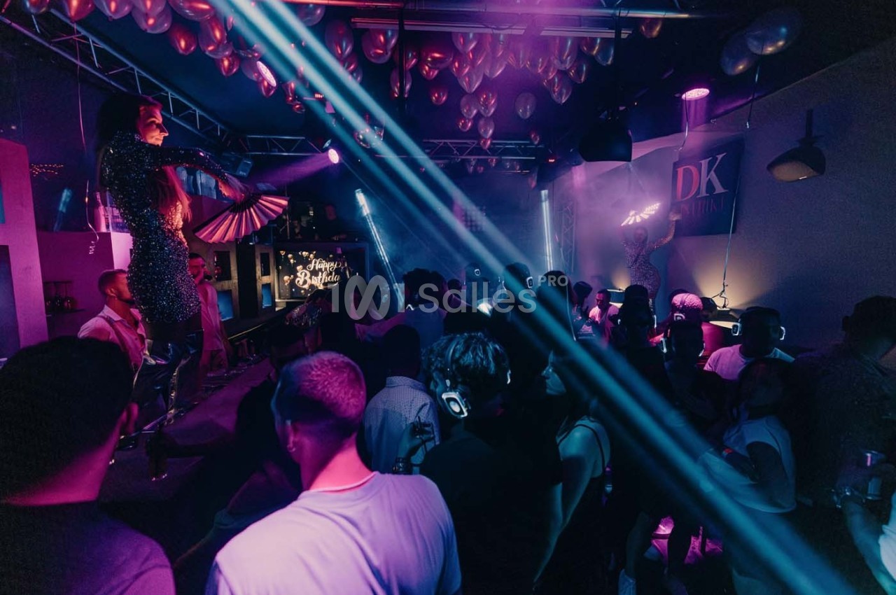Des personnes dansent dans une salle de fête sombre avec éclairages colorés et artistes sur scène.