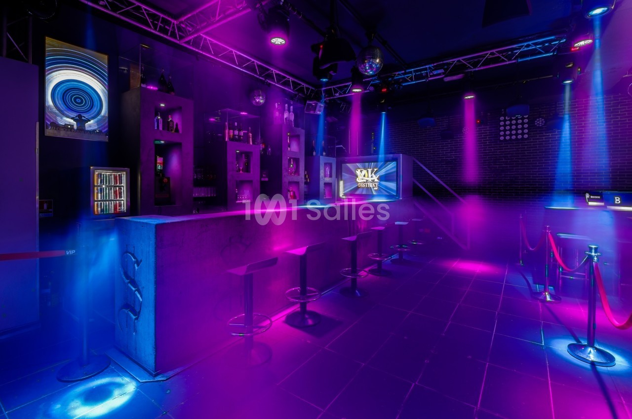 Intérieur d'une discothèque avec bar, tabourets, éclairage coloré et ambiance nocturne.