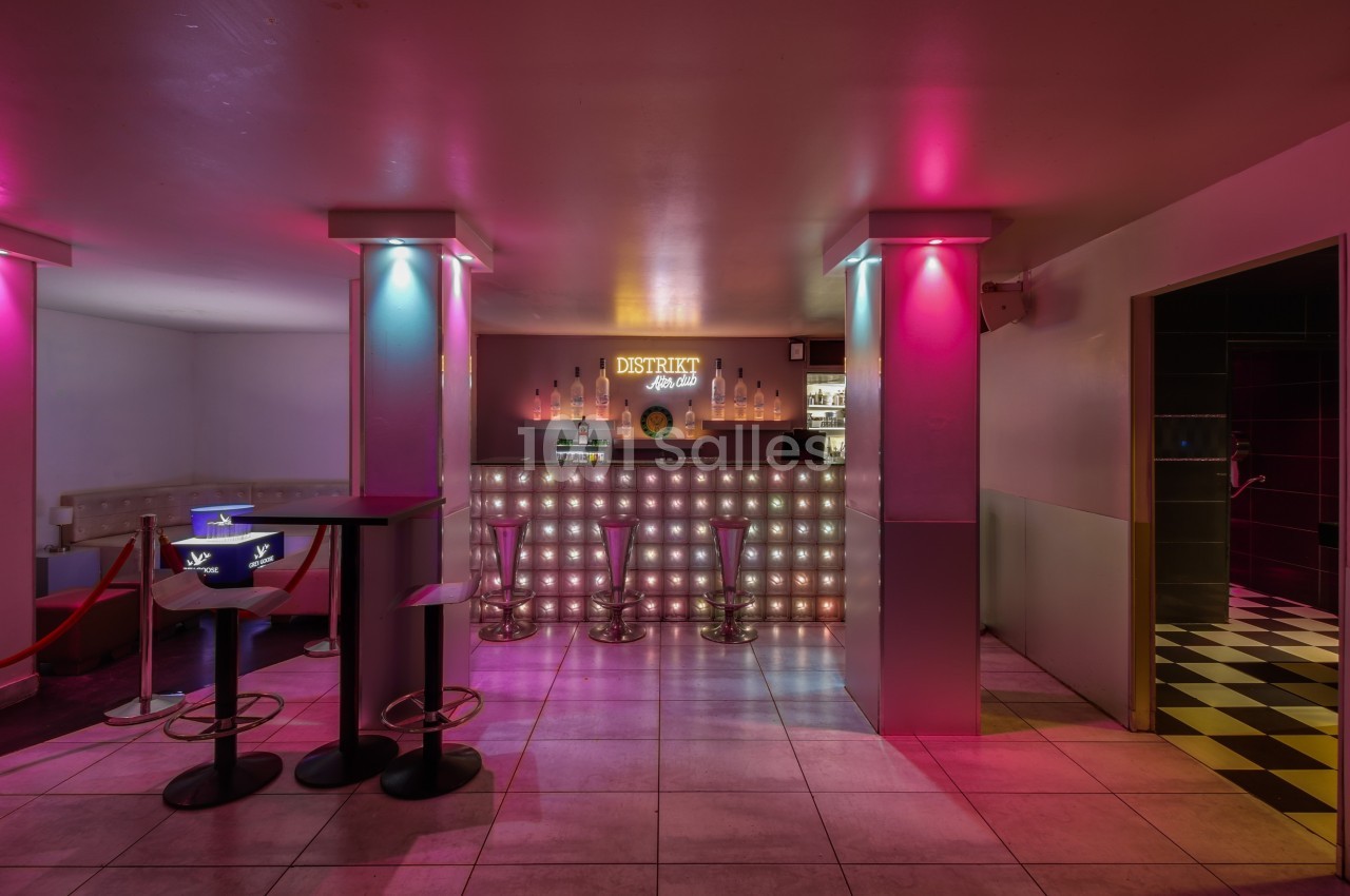 Bar lumineux avec tabourets hauts, éclairage rose et bleu, et comptoir rétroéclairé dans un espace moderne.